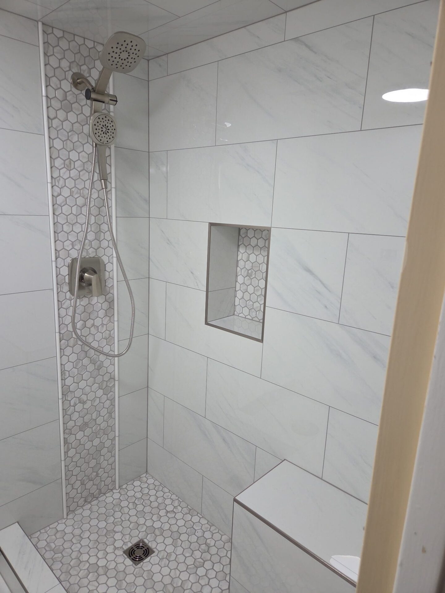 Finished marble-look tile shower surround with hexagon accent stripe and built-in niche